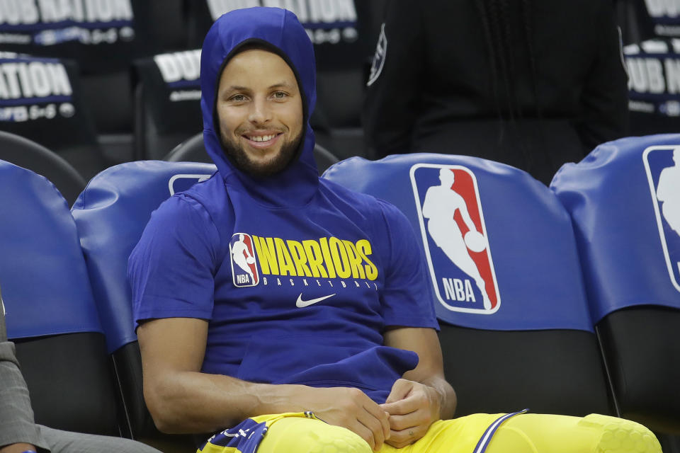 Golden State Warriors guard Stephen Curry smiles on the bench as players warm up before an NBA basketball game between the Warriors and the Los Angeles Lakers in San Francisco, Thursday, Feb. 27, 2020. (AP Photo/Jeff Chiu)