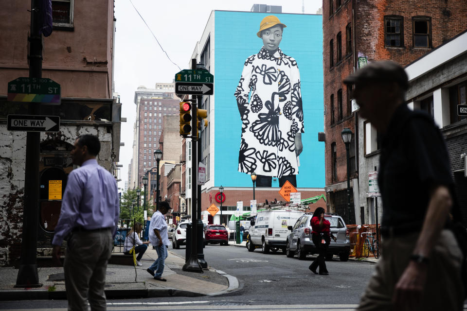 In this Tuesday, June 18, 2019 photo, pedestrians walk near a Mural Arts Philadelphia mural of Najee Spencer-Young by artist Amy Sherald by in Philadelphia. Sherald is the artist who painted the official portrait of Michelle Obama. (AP Photo/Matt Rourke)