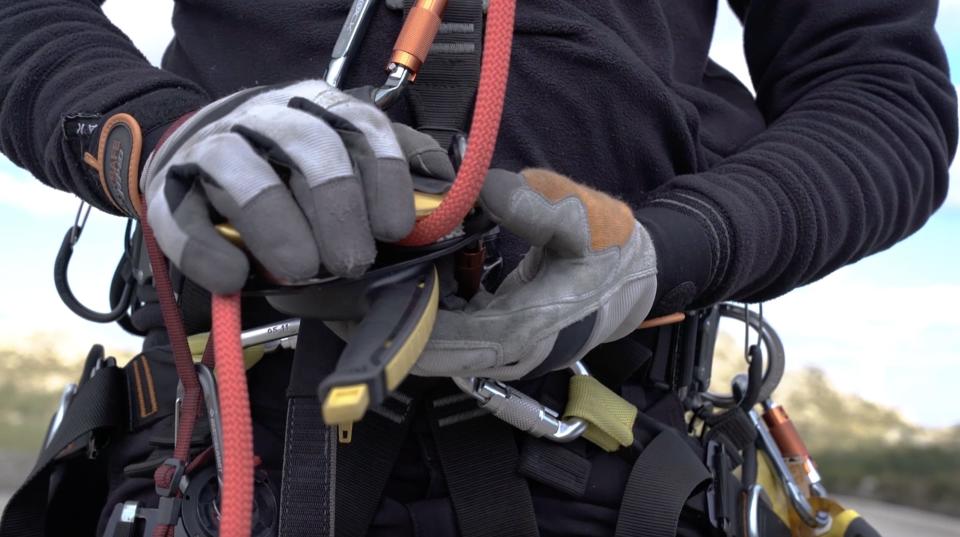 Sardo, wearing gloves, checks his harness to make sure it is properly attached to the cable.