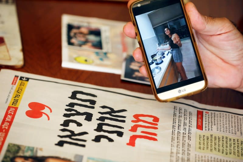 Israel, the uncle of Naama Issachar, shows a photo of Naama on his mobile phone next to a newspaper with an article about her at his home in Rehovot