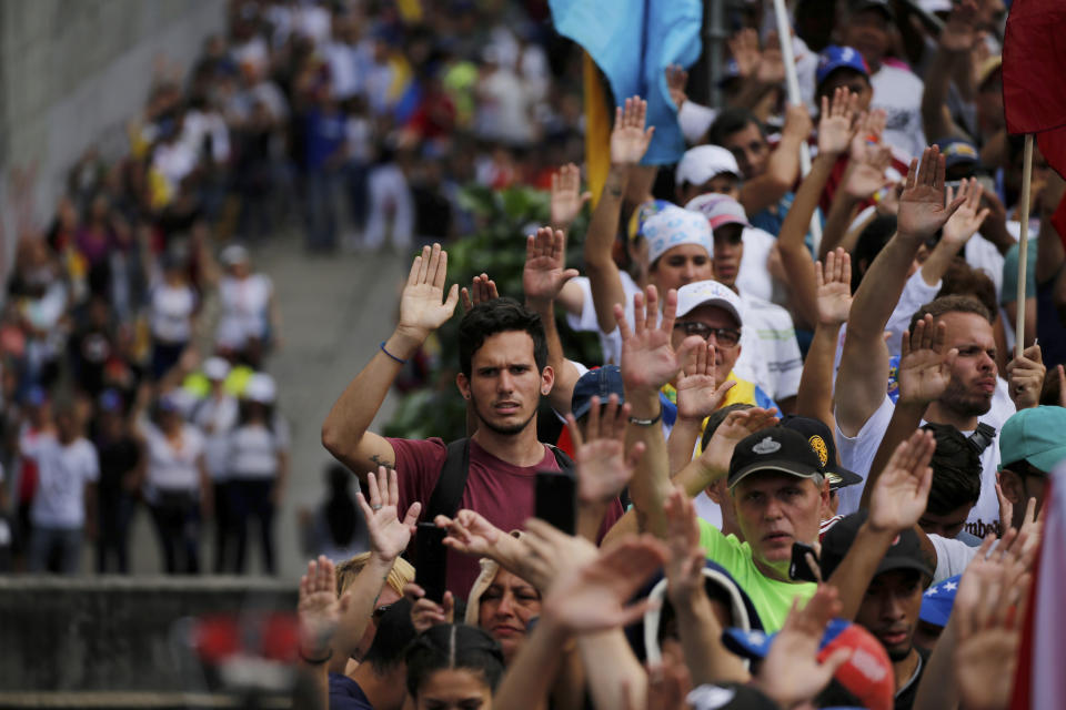 Anti-government protesters hold their hands up during the symbolic swearing-in of Juan Guaido, head of the opposition-run congress, who declared himself interim president of Venezuela, during a rally demanding President Nicolas Maduro's resignation in Caracas, Venezuela, Wednesday, Jan. 23, 2019. (AP Photo/Fernando Llano)