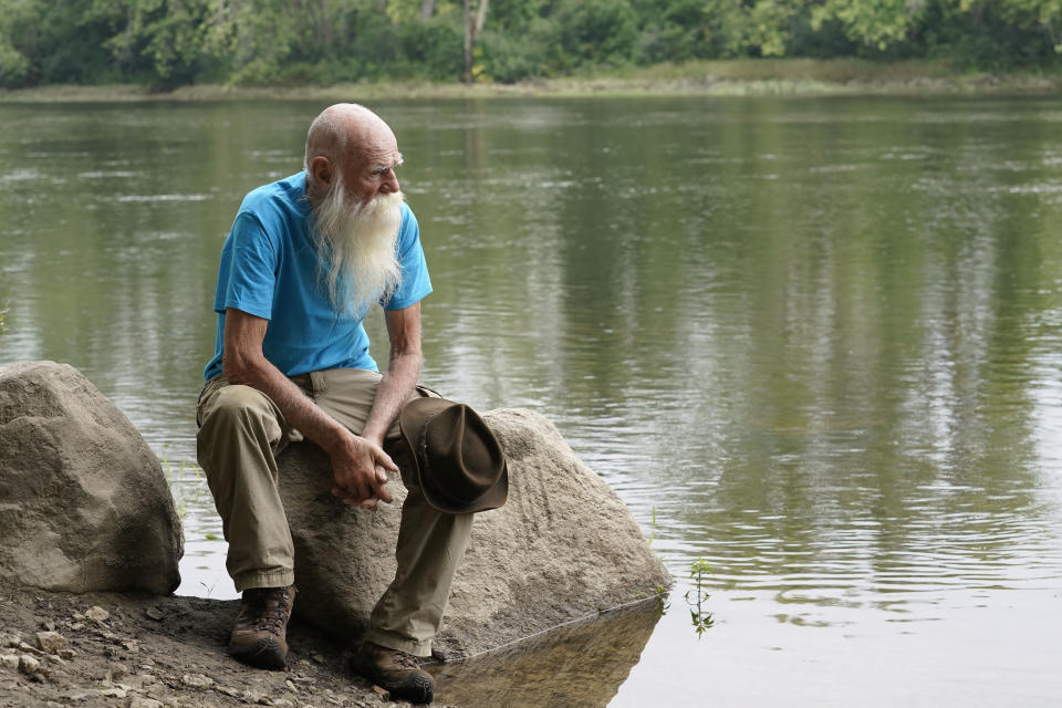 FILE — David Lidstone, 81, sits for a photograph near the Merrimack River, Tuesday, Aug. 10, 2021, in Boscawen, N.H. Lidstone, an off-the-grid New Hampshire hermit known to locals as "River Dave," had been living in a cabin in the woods along the Merrimack River, in Canterbury, N.H., for nearly three decades. A contempt of court hearing has been scheduled for Thursday, March 31, 2022, for Lidstone, accused of returning to live on property that he was ordered to stay away from. (AP Photo/Steven Senne, File)