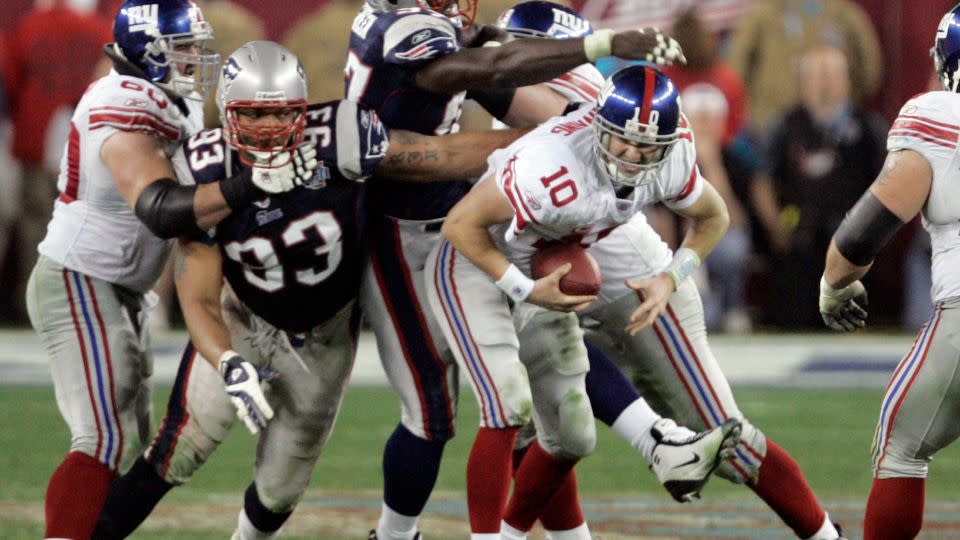 New York Giants quarterback Eli Manning scrambles away from New England Patriots defenders before launching a 32-yard pass to David Tyree with 1:15 left in the Super Bowl in 2008. - Elaine Thompson/AP