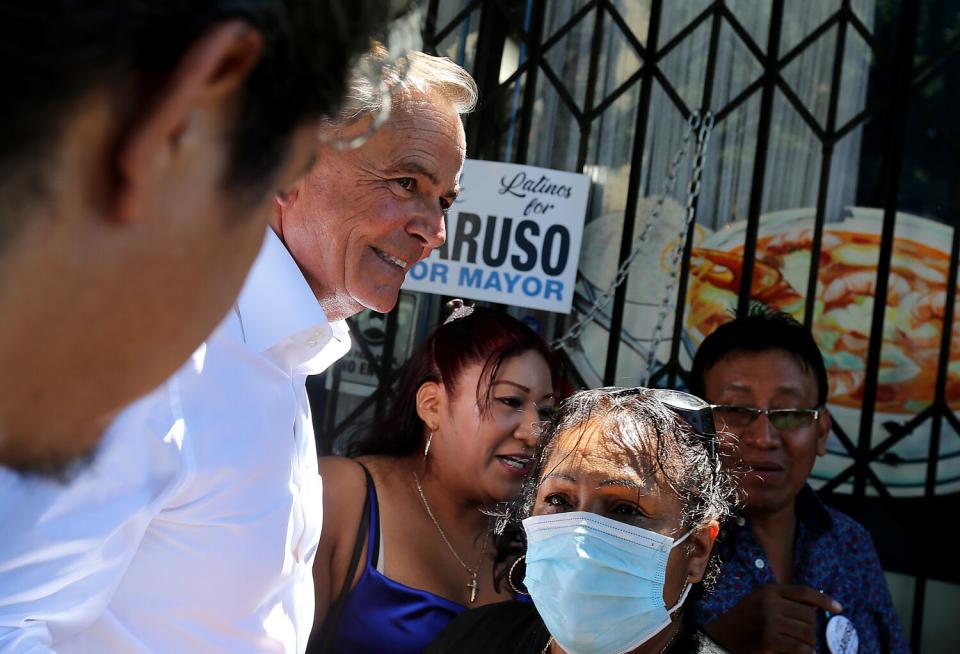 A smiling man is surrounded by a few people in front of a gated shop.