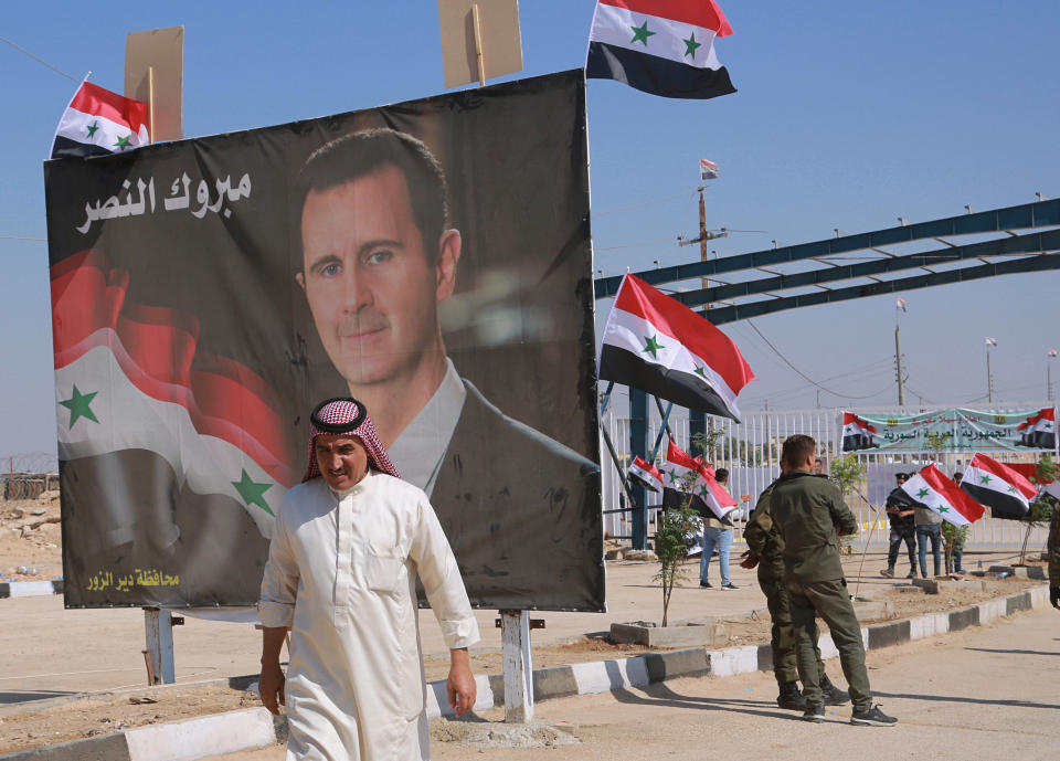 FILE - In this Sept. 30, 2019, file photo, a man passes a poster of Syrian President Bashar Assad with Arabic that reads, "Congratulations victory," while crossing the border into Syria at the newly opened crossing between the Iraqi town of Qaim and Syria's Boukamal, Syria. Assad has snapped up a prize from world powers that have been maneuvering in his country’s multifront wars. Without firing a shot, his forces are returning to towns and villages in northeastern Syria where they haven’t set foot for years. (AP Photo/Hadi Mizban, File)