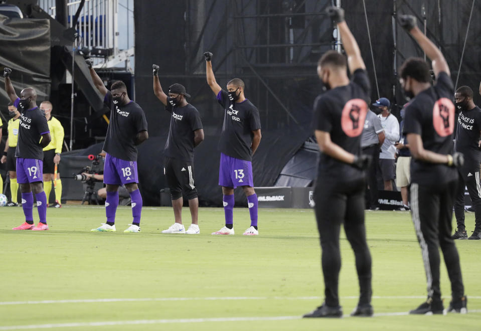 Jugadores del Orlando City (izquierda) levantan un puño como una protesta contra la injusticia social, el miércoles 8 de julio de 2020, en Kissimmee, Florida, antes de poner en marcha un torneo que marca la reanudación de la actividad en la MLS, interrumpida por la pandemia de coronavirus (AP Foto/John Raoux)