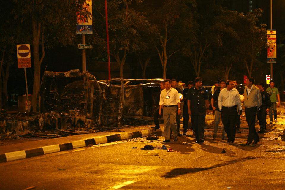 Singapore's Deputy Prime Minister Teo Chee Hean (front R) and Minister in Prime Minister's Office S Iswaran (front 2nd R) look at the site of two burnt vehicles following a riot in Singapore's Little India district, December 9, 2013. A crowd set fire to vehicles and clashed with police in the Indian district of Singapore late on Sunday, in a rare outbreak of rioting in the city state. Television footage showed a crowd of people smashing the windscreen of a bus, and at least three police cars being flipped over. The Singapore Police Force said the riot started after a fatal traffic accident in the Little India area. REUTERS/Rob Dawson (SINGAPORE - Tags: CIVIL UNREST POLITICS)