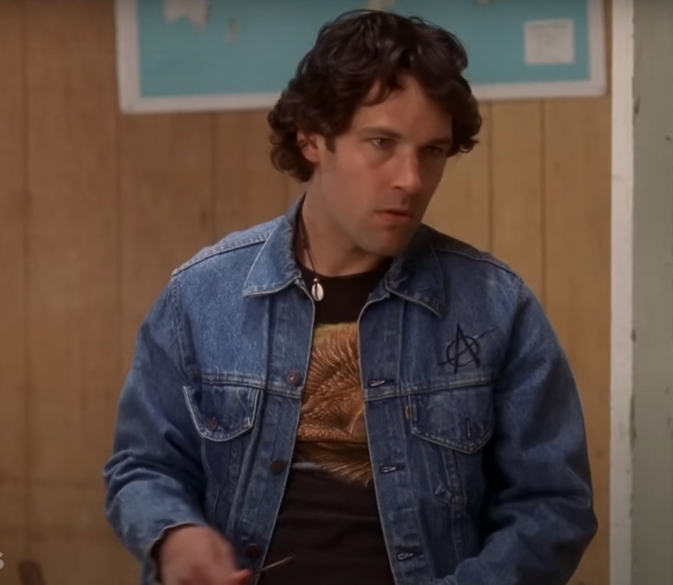 Andy in denim jacket over sweater, standing indoors, concerned expression