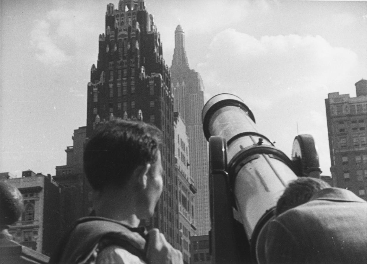 Tourists at Bryant Park looking through a telescope towards American Radiator Building and the Empire State Building, New York City, 1929.