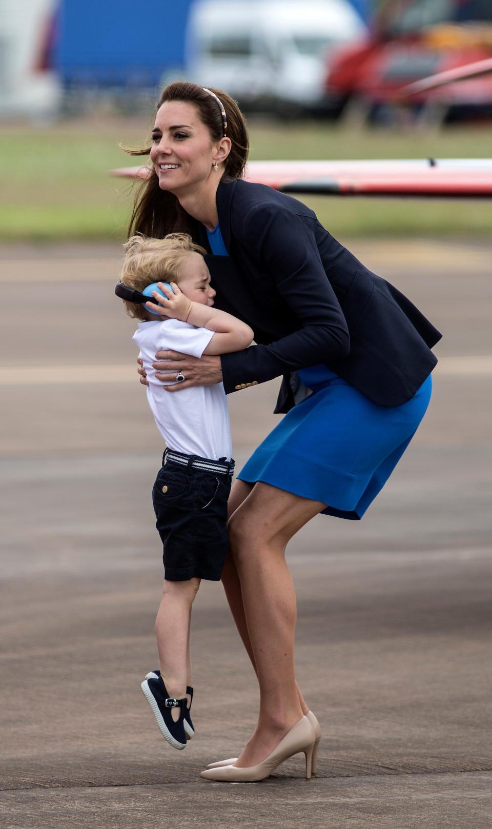 Kate Middleton picks up Prince George, who is covering his ears with headphones.