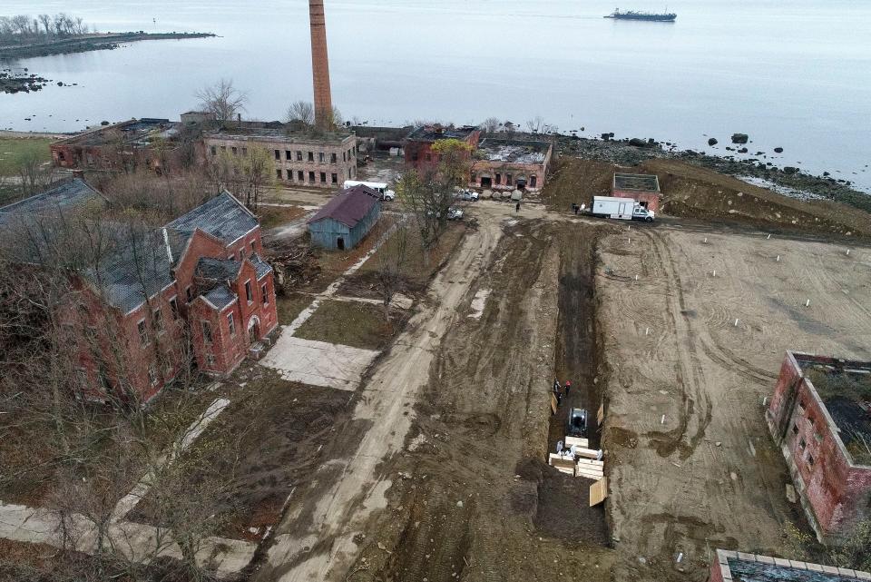 Workers wearing personal protective equipment bury bodies in a trench on Hart Island, Thursday, April 9, 2020, in the Bronx borough of New York. On Thursday, New York City’s medical examiner confirmed that the city has shortened the amount of time it will hold on to remains to 14 days from 30 days before they will be transferred for temporary internment at a City Cemetery.