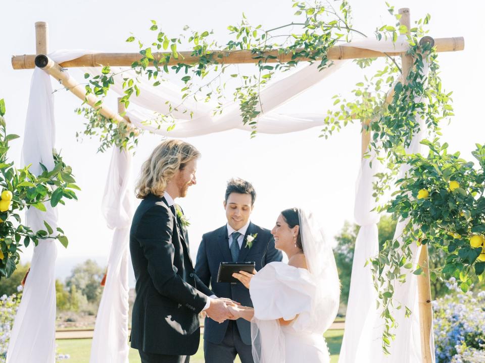 A bride and groom hold hands at the altar as their officiant reads to them.