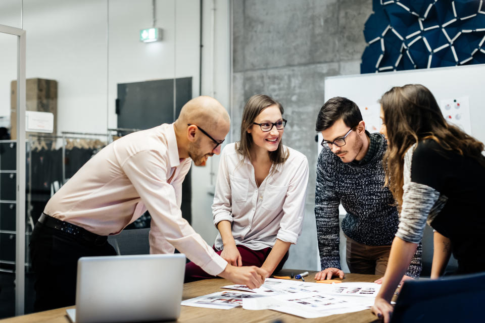 Microfeminism A team of four business people is standing in front a desk in a bright office room. They ambitiously point at documents while smiling and looking at the charts and notes.