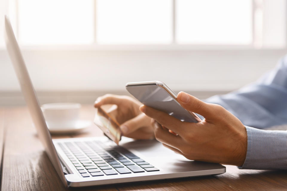 Modern technologies concept. Unrecognizable male booking tickets online preparing for business trip, using smartphone and holding credit card. Closeup