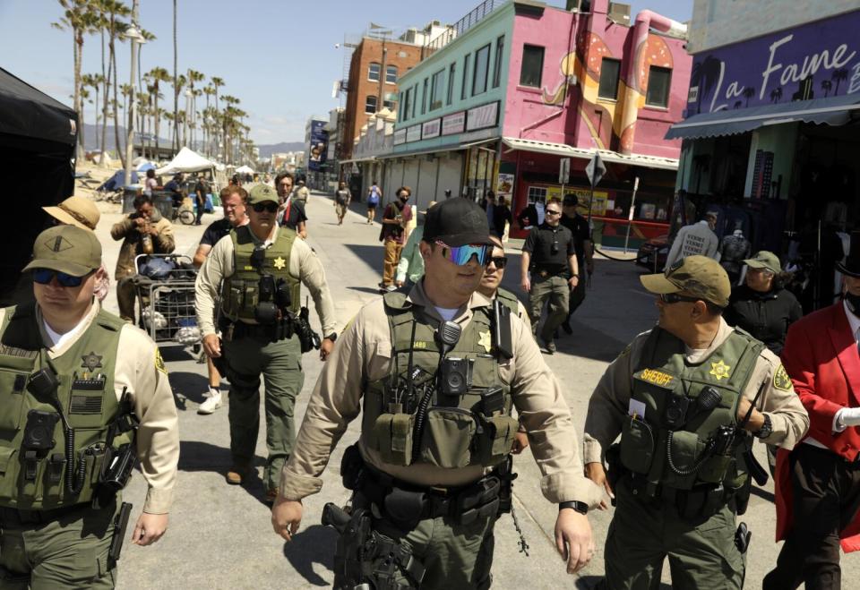 Deputies wearing uniforms, vests and hats patrol a beachfront boardwalk