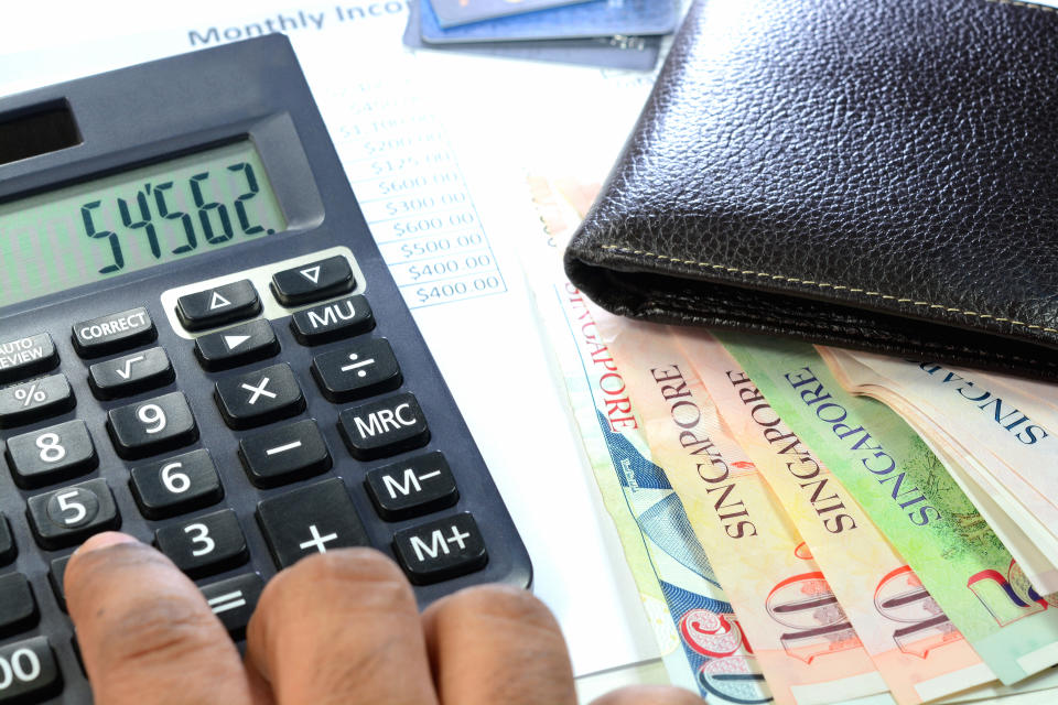 Singapore currency notes, wallet and calculator on a desk, illustrating a story on paying taxes on withdrawals from Supplementary Retirement Scheme (SRS) in Singapore.