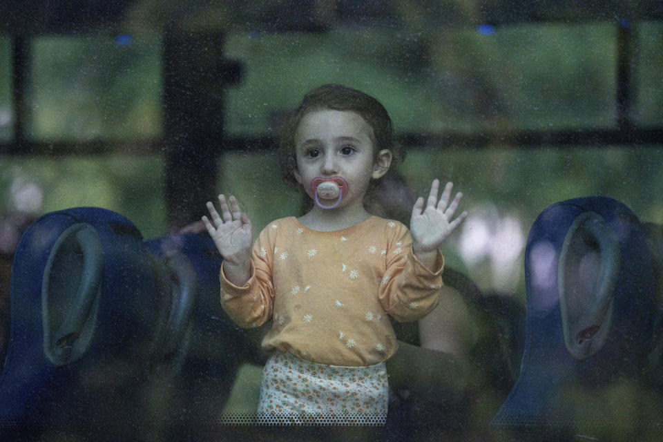 A young girl looks through a bus window as her family departs the northern Israeli city of Kiryat Shmona, Israel, Friday, Oct. 20, 2023. The Israeli military announced Friday it would evacuate the border city a day after three residents were injured by cross-border fire from militants in Lebanon. (AP Photo/Baz Ratner)