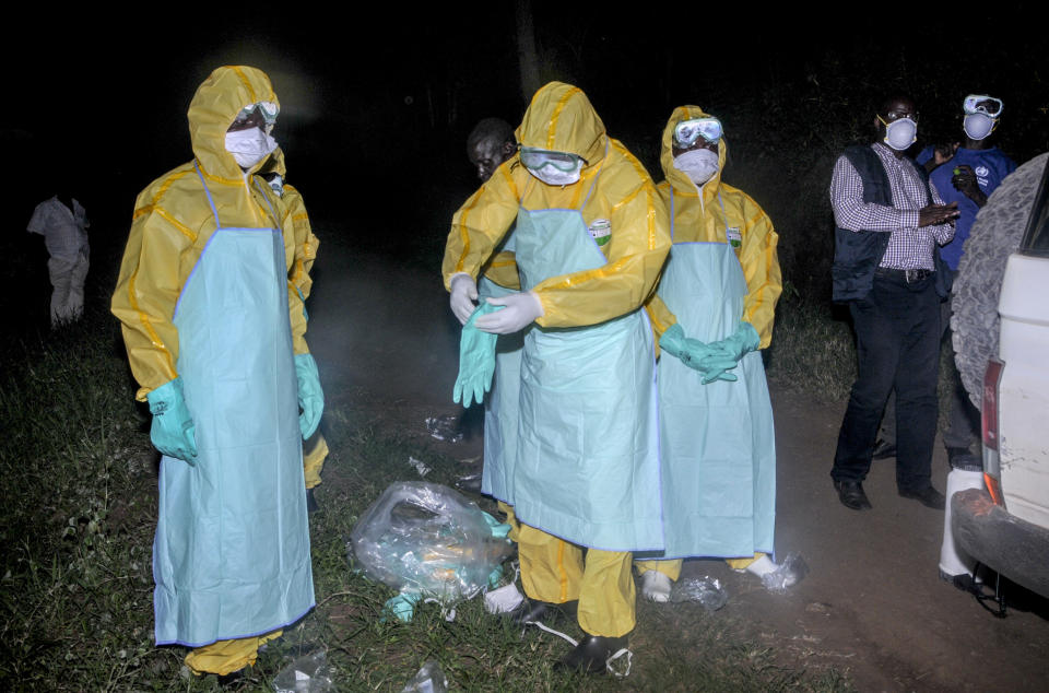 Workers wearing protective clothing prepare to bury Agnes Mbambu who died of Ebola, the 50-year-old grandmother of the 5-year-old boy who became Ebola's first cross-border victim, in the village of Karambi, near the border with Congo, in western Uganda Thursday, June 13, 2019. The two were part of a larger Congolese-Ugandan family who crossed to Congo when one of their elders there, a pastor, became sick with Ebola and they crossed back into Uganda on June 9 via a footpath not patrolled by border authorities. (AP Photo/Ronald Kabuubi)