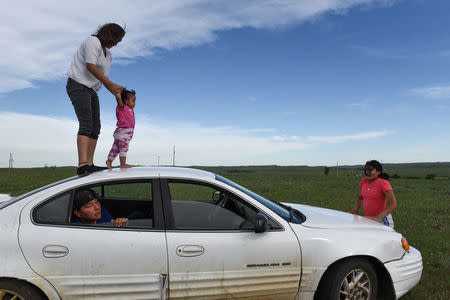 Angel Lookinghorse walks her younger cousin on top of her car while other family members sit and stand near the car on the Cheyenne River Reservation in Green Grass, South Dakota, U.S., May 30, 2018. REUTERS/Stephanie Keith