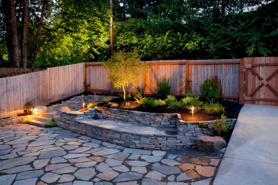 Tiered patio in backyard at dusk surrounded by landscaping and spot lighting