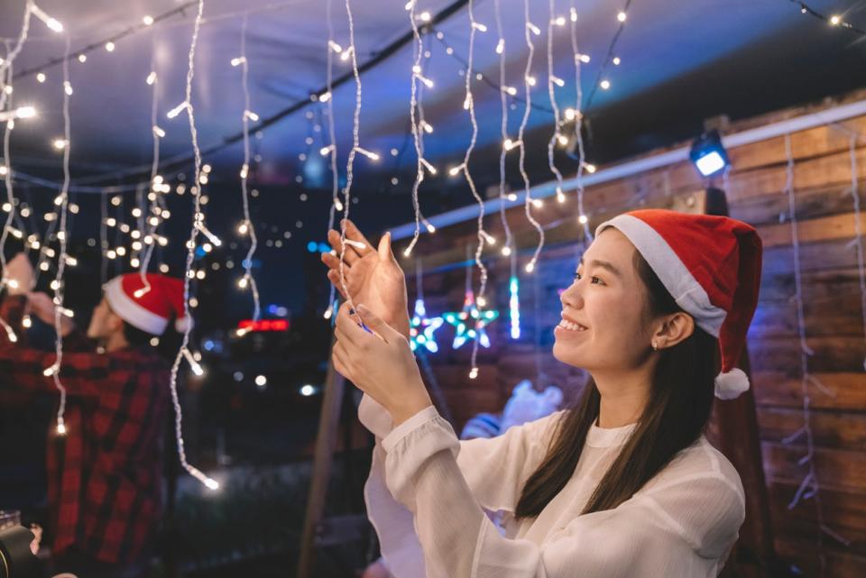 Young woman wearing Santa hat admiring icicle string lights hanging from ceiling.