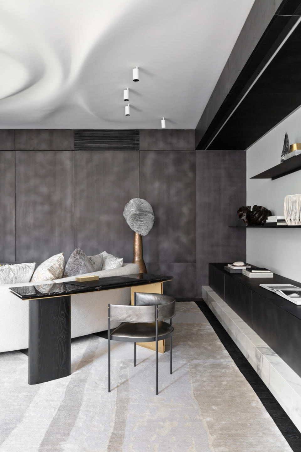 A cool living room scheme with grey textured walls, white and cream carpet, black console table and metallic leather chair