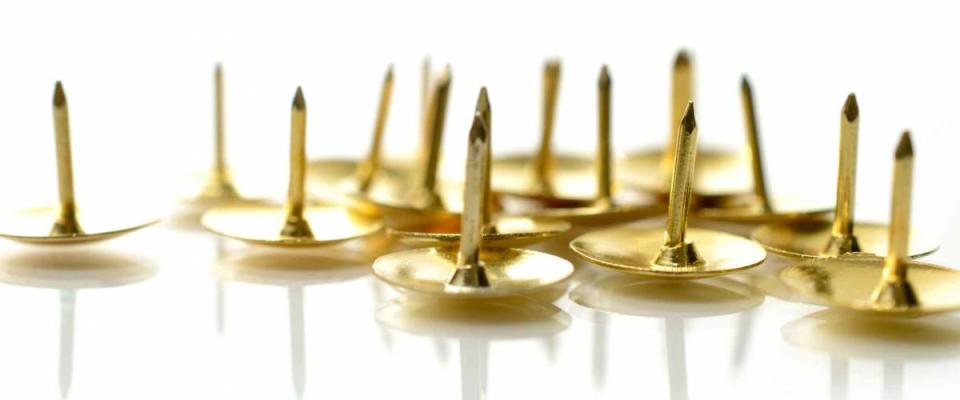 Office concept stock photograph. Studio macro of metal tacks on a white surface. Copy space.