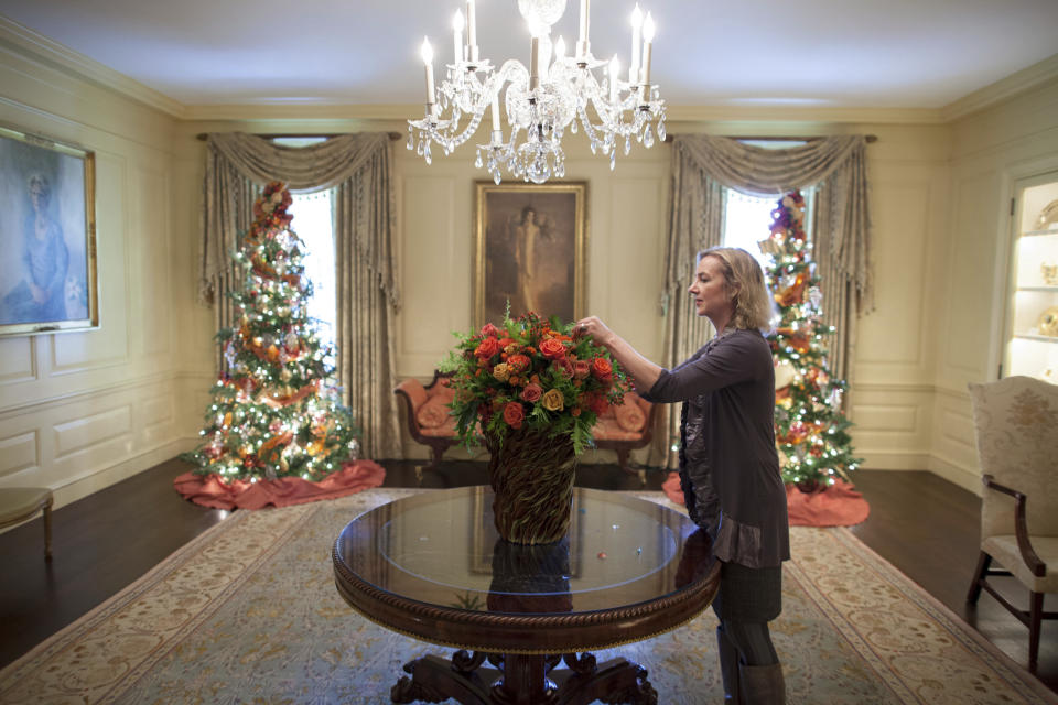 In this Dec. 1, 2010 photo provided by Stichting Kunstboek, Laura Dowling completes a holiday arrangement of peach and coral roses in a magnolia leaf vase in the Vermeil Room, before the launch of the White House Christmas season, with the Aaron Shikler portrait of First Lady Jacqueline Kennedy in the background at the White House in Washington. The photograph is featured in the book "Floral Diplomacy: At the White House," by Laura Dowling. (Chuck Kennedy/The White House/Stichting Kunstboek via AP)