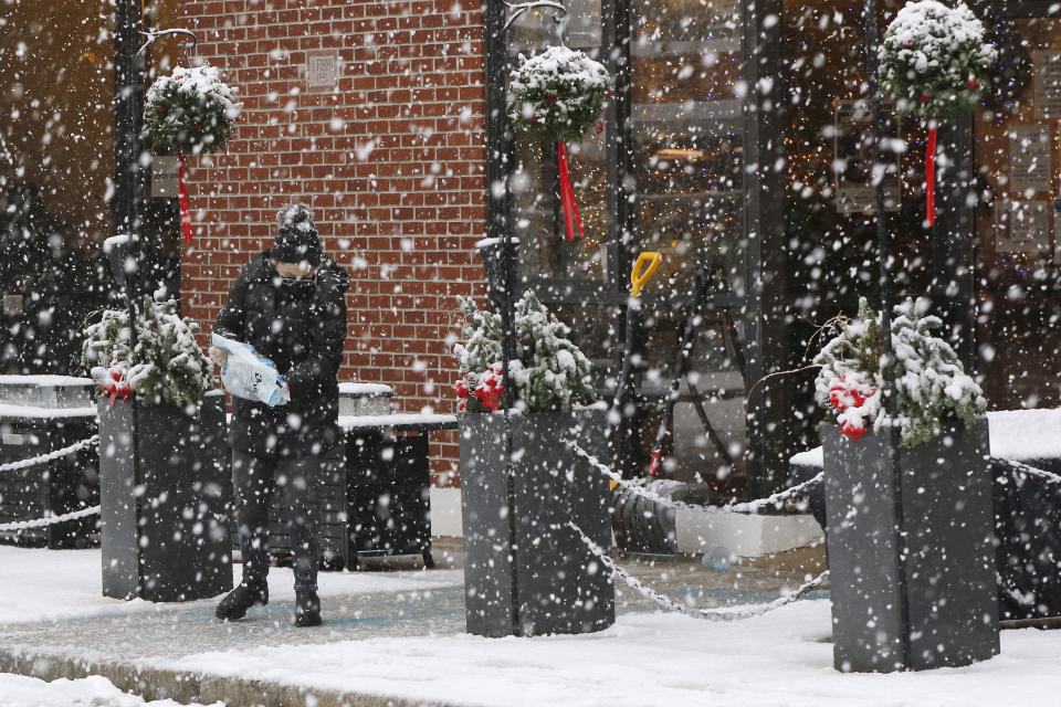 A worker pours ice melting pellets on the walkway outside a restaurant, Saturday, Dec. 5, 2020, in downtown Marlborough, Mass. The northeastern United States is seeing the first big snowstorm of the season. (AP Photo/Bill Sikes)