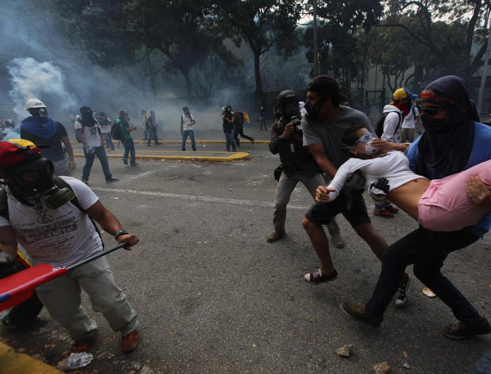 A female demonstrator is carried away after being overwhelmed by tear gas fired by Bolivarian National Police during clashes at an antigovernment protest in Caracas, Venezuela, Wednesday, March 12, 2014. According to local authorities, several deaths have been reported Wednesday, and a number of others, including National Guardsmen, have been wounded after being shot by unknown assailants in separate incidents in the central Venezuelan city of Valencia. (AP Photo/Fernando Llano)