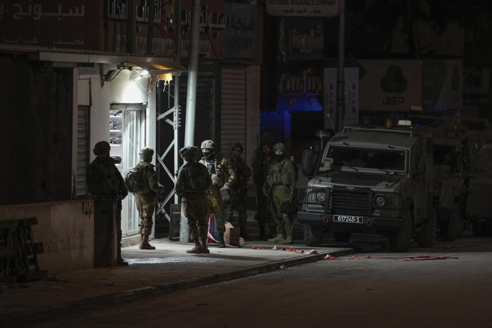 Israeli soldiers are deployed at the scene where a Palestinian gunman opened fire at soldiers in the West Bank town of Hawara, Saturday, March 25, 2023. The Israeli military said two soldiers were wounded Saturday evening in a drive-by shooting in the occupied West Bank, the latest in months-long violence between Israel and the Palestinians. The attack was the third to take place in the Palestinian town of Hawara in less than a month. A manhunt was launched as forces sealed roads leading to Hawara. (AP Photo/Majdi Mohammed)