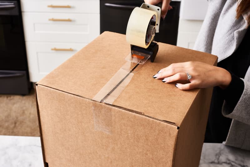 A tape roller goes across the bottom of a cardboard box to prepare for a move