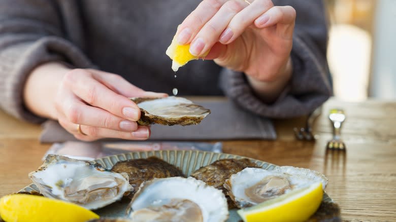 Person squeezing lemon on oysters