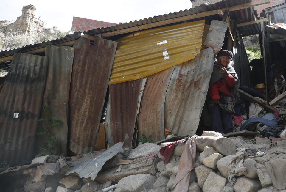 In this May 13, 2020 photo, 80-year-old Dominga Aduviri looks out from her makeshift home as she watches her "adopted" grandson Wilmer Gutierrez arrive with a bag of donated food, in La Paz, Bolivia. The government has arranged for aid packages for the elderly, but many poor Bolivians cannot collect them for various reasons. (AP Photo/Juan Karita)