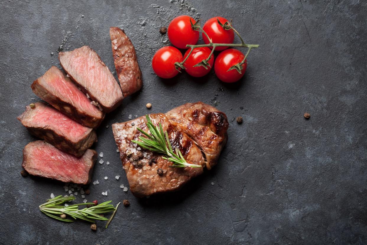 Grilled sliced beef steak and tomatoes on stone table. Top view