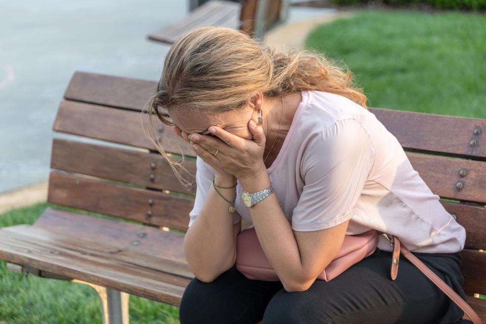 woman crying into her hands on a park bench