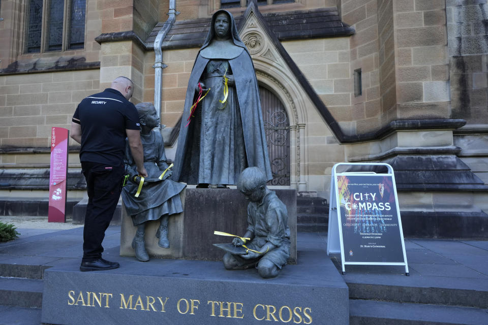 A security guard removes ribbons left by protesters as a symbol of support to sex abuse victims tied to a statue of Saint Mary MacKillop at St. Mary's Cathedral where Cardinal George Pell's coffin will be brought to lay in state in Sydney, Wednesday, Feb. 1, 2023. Pell, who was once considered the third-highest ranking cleric in the Vatican and spent more than a year in prison before his child abuse convictions were squashed in 2020, died in Rome last month at age 81. (AP Photo/Rick Rycroft)