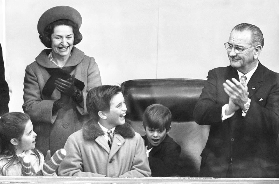 FILE_ Children of Peace Corps Director R. Sargent Shriver joined President Johnson and Lady Bird Johnson in the inaugural reviewing stand at the White House during the Jan. 20, 1965 parade. From left are Maria, Robert, center, and Timothy Shriver. Tommy takes over the president's chair. Lady Bird Johnson's own voice is helping offer new looks at the former first lady in several recent projects. Johnson began recording an audio diary in the tumultuous days after her husband, Lyndon B. Johnson, became president following the assassination of President John F. Kennedy in 1963. (AP Photo/File)