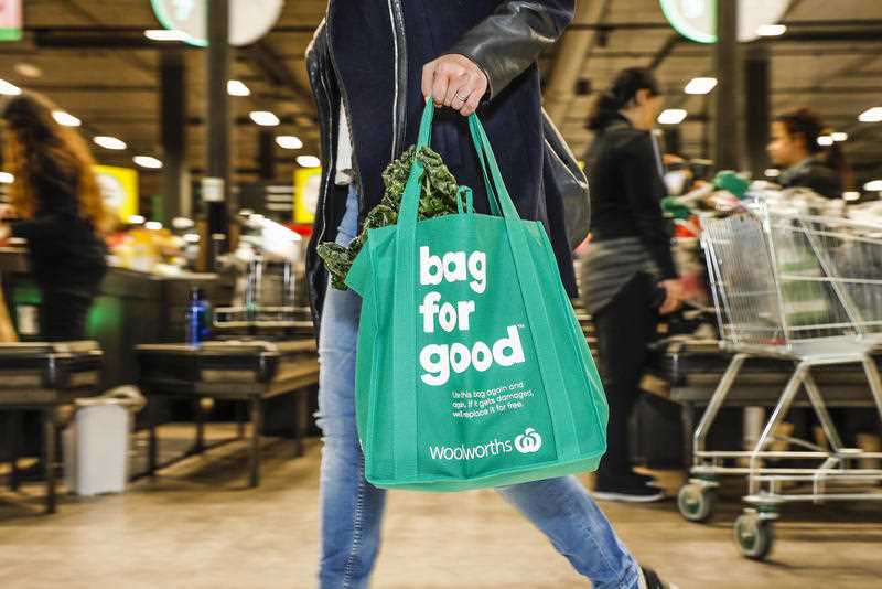 A woman carries a Woolworths reusuable bag through the supermarket.