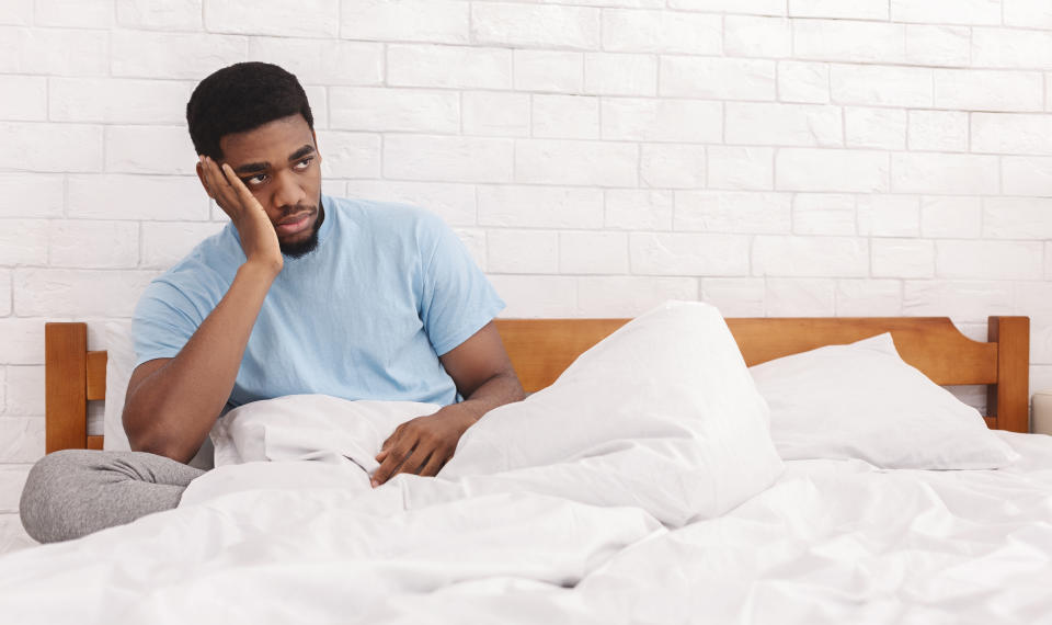 Sad young black guy sitting in bed, thinking about relationship problems, considering breaking up with girlfriend, copy space