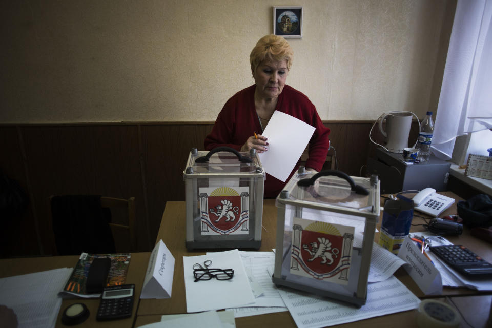 A Ukrainian woman, who is a member of the district electoral committee, makes final preparations as she stands next to ballot boxes for Sunday's referendum at a polling station in Simferopol, Ukraine, Saturday, March 15, 2014. Tensions are high in the Black Sea peninsula of Crimea, where a referendum is to be held Sunday on whether to split off from Ukraine and seek annexation by Russia. (AP Photo/Manu Brabo)