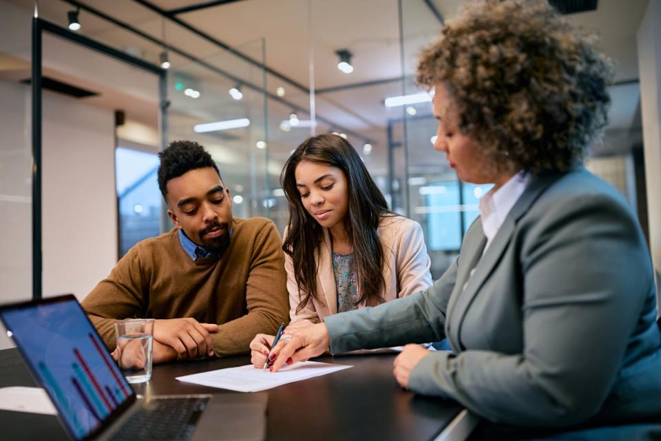 Three people sit at an office desk looking at a document. 