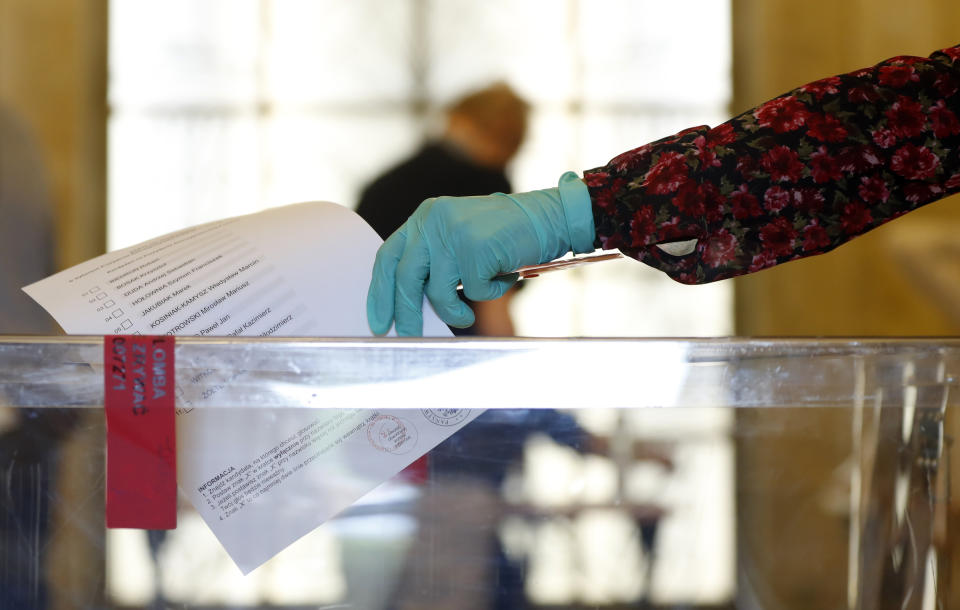 A resident, wearing protective gloves, casts a vote during presidential election in Warsaw, Poland, Sunday, June 28, 2020. The election will test the popularity of incumbent President Andrzej Duda who is seeking a second term and of the conservative ruling party that backs him. (AP Photo/Petr David Josek)