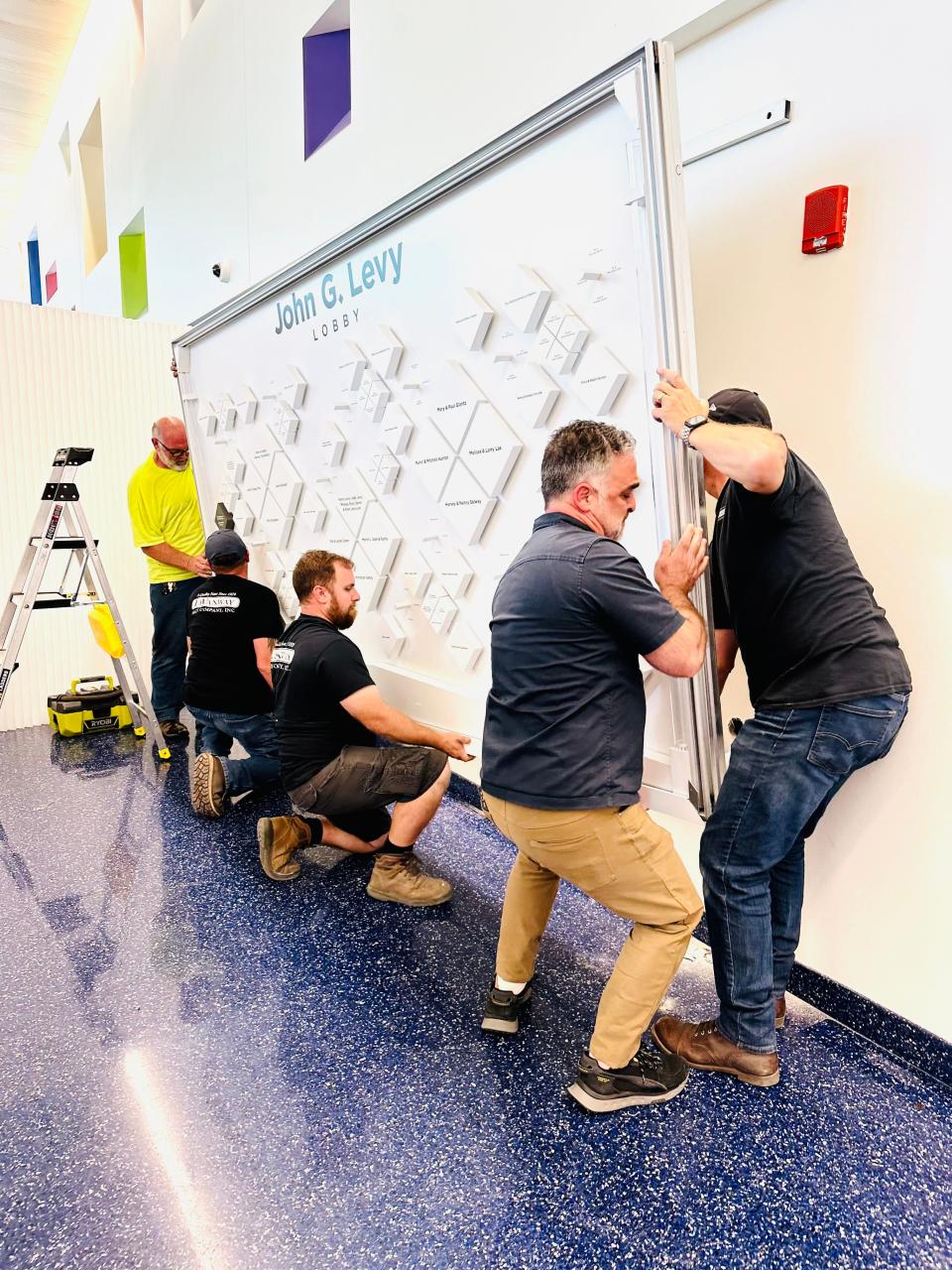 Staffers from LaVanway Sign Company of Southfield and Ferndale display company Echo Charlie lift a new interactive wall into place at Children’s Hospital of Michigan on Tuesday afternoon. The wall is the key feature of what’s being dedicated as the John G. Levy Lobby.