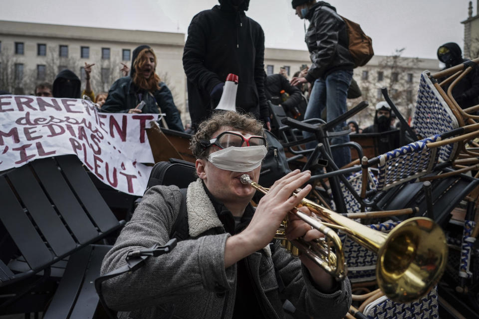 A man plays the trumpet in front of a barricade during a demonstration in Lyon, central France, Tuesday, March 7, 2023. Demonstrators were marching across France on Tuesday in a new round of protests and strikes against the government's plan to raise the retirement age to 64, in what unions hope to be their biggest show of force against the proposal. (AP Photo/Laurent Cipriani)