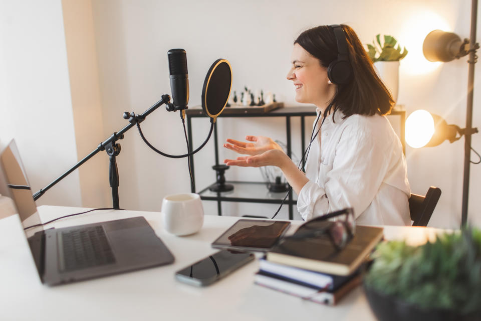 Host at her beautiful home office sitting down at the desk. The woman is in the middle of a live show or recording a podcast. She is joyful, lauighing, enjoying herself.
