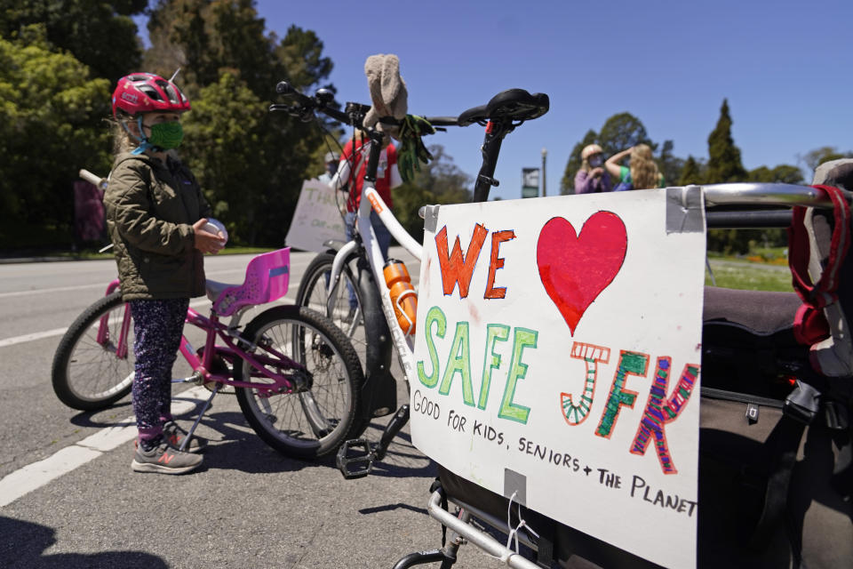 Luna Darr, 5, stands by her bike along with her father's during a celebration to mark the one-year anniversary of car-free John F. Kennedy Drive in Golden Gate Park, Wednesday, April 28, 2021, in San Francisco. At the start of the pandemic, San Francisco closed off parts of a major beachfront highway and Golden Gate Park to cars so that people had a safe place to run and ride bikes. Open space advocates want to keep those areas car-free as part of a bold reimagining of how U.S. cities look. But opponents decry the continued closures as elitist, unsafe and nonsensical now that the pandemic is over and people need to drive again. (AP Photo/Eric Risberg)