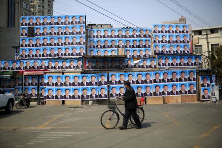 A man with a bicycle walks past a building covered in posters of Chinese President Xi Jinping in Shanghai, China, March 26, 2016. REUTERS/Aly Song/File Photo