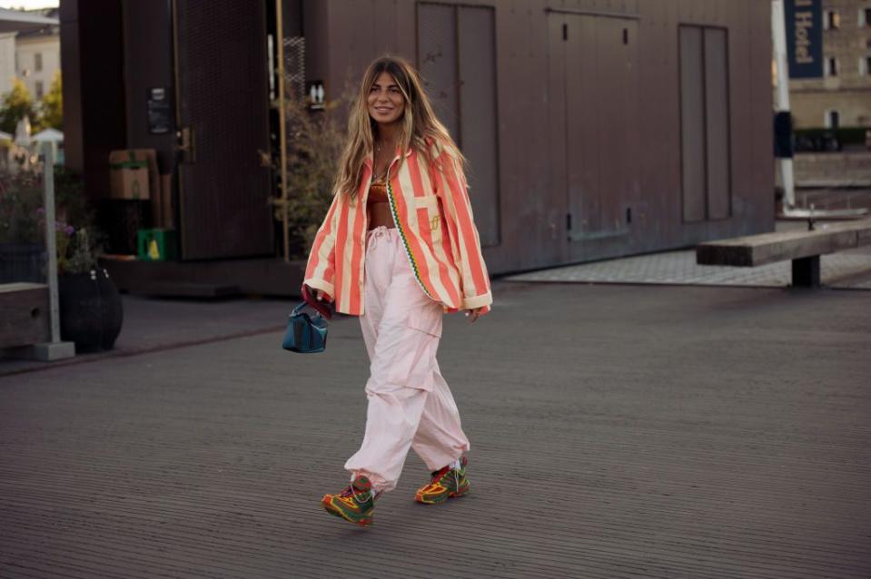 copenhagen, denmark august 11 a guest wearing light pink cargo pants, orange swimsuit top, orange and pale yellow striped shirt, yellow, red and green sneakers posing outside ganni during copenhagen fashion week springsummer 2023 on august 11, 2022 in copenhagen, denmark photo by raimonda kulikauskienegetty images