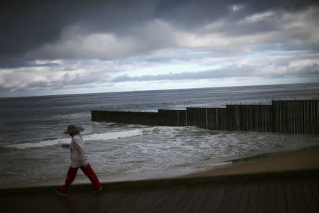 A woman walks past a section of the current border fence separating Mexico and the United States in this picture taken from the Mexican side of the border in Tijuana, Mexico March 14, 2018. REUTERS/Edgard Garrido/Files